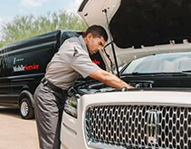 Técnico realizando el mantenimiento de vehículo con el capó levantado cerca de la van de Mobile Service