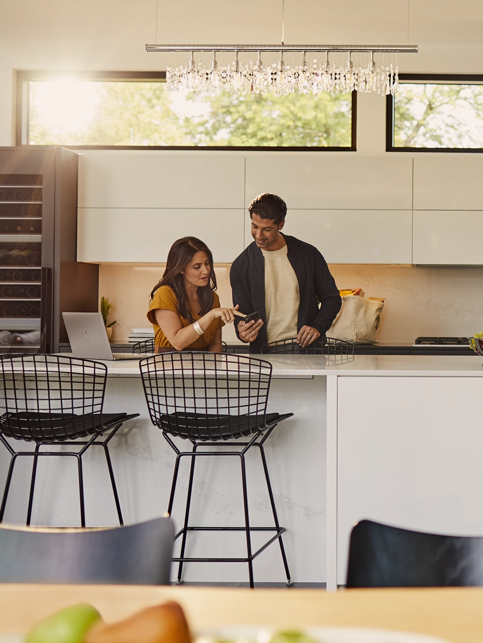 A man and woman standing in the kitchen and lookin at a phone.